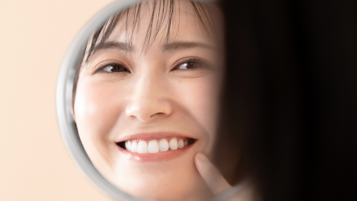 白くなった歯を鏡で見て満足してほほ笑む女性